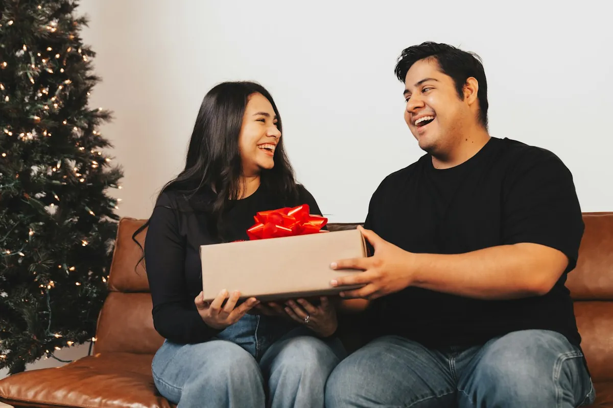 A couple laughing on a couch with a wrapped present